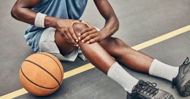 Athlete sitting on ground grabbing knee
